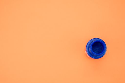 A top view of a small opened can of blue gouache paint isolated on a coral background