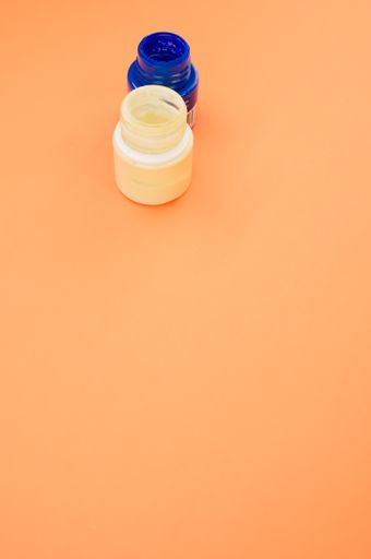 A vertical shot of small opened cans of blue and white gouache paints isolated on a coral background