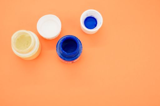 A top view of small opened cans of blue and white gouache paints isolated on a coral background