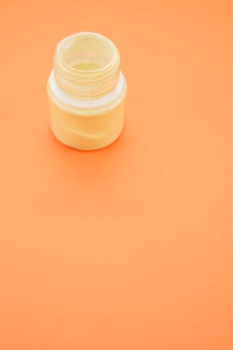 A vertical sho of a small opened can of white gouache paint isolated on a coral background