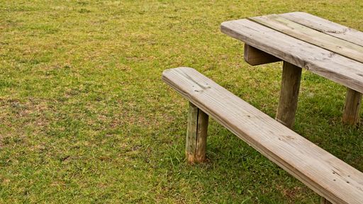 A high angle shot of a wooden table and a bench on the grass covered field