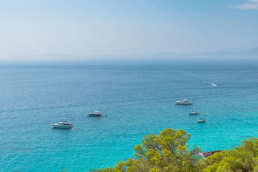 Boats anchored near the shore of a cala with crystal clear turquoise waters on the island of Mallorca, Spain.
