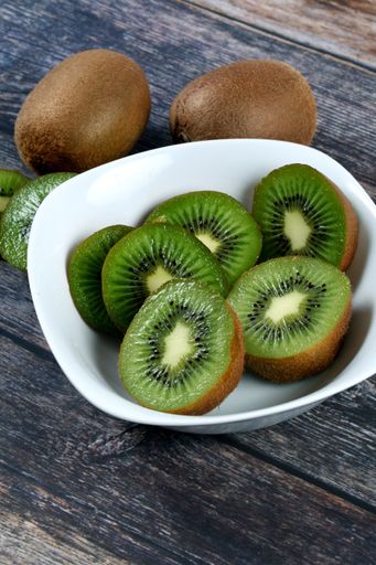 A vertical shot of a bowl filled with slices of fresh kiwi on a wooden surface