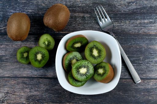 A high angle shot of a bowl filled with slices of fresh kiwi on a wooden surface