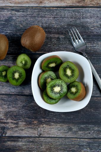 A vertical shot of a bowl filled with slices of fresh kiwi on a wooden surface