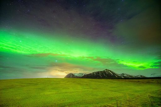 A breathtaking view of Aurora Borealis over the field and snow-covered mountains