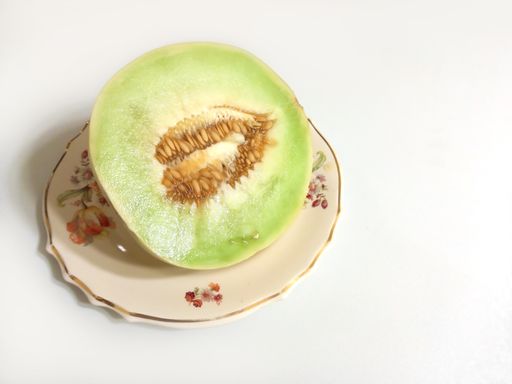 high angle shot of half a creamy yellow green ripe sweet juicy pulpy melon (cucumis melo) on a plate on a white background with copyspace