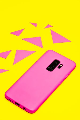 A vertical shot of a pink mobile phone on a yellow surface surrounded by triangles