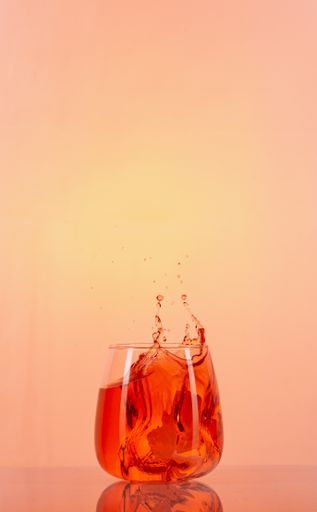 A vertical shot of a refreshing cocktail with splash on delicate peach background