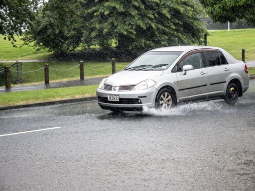 A car driving through a puddle on a wet street next to the sidewalk