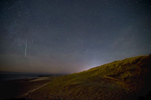 A breathtaking beach scene at night, illuminated by a starlit sky with shooting stars over the North Sea in Denmark