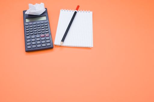 A scientific calculator, pencil, grid notepad and a crumpled paper isolated on an orange background