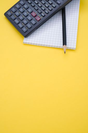 A vertical shot of a scientific calculator, pencil and grid notepad isolated on a yellow background with space for your text