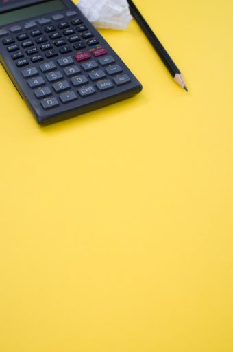 A vertical shot of a scientific calculator, pencil, grid notepad and a crumpled paper isolated on a yellow background with space for your text