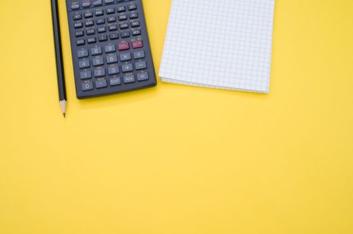 A partial view of a scientific calculator, pencil, and a grid notepad isolated on a yellow background