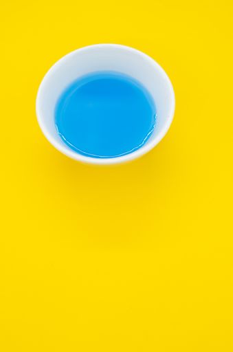 A vertical shot of a paint rinsing bowl with blue-stained water on a yellow surface