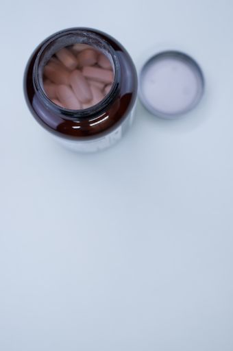 A vertical shot of an uncapped bottle of tablets on a white surface with space for your text