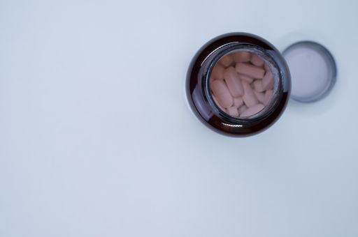 An overhead shot of an uncapped bottle of tablets on a white surface with space for your text