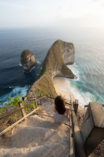 A back view of a woman standing on stairs and enjoying the view of the ocean, Bali, Indonesia