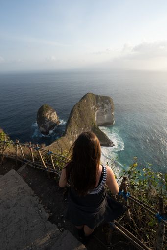 A back view of a woman standing on stairs and enjoying the view of the ocean, Bali, Indonesia