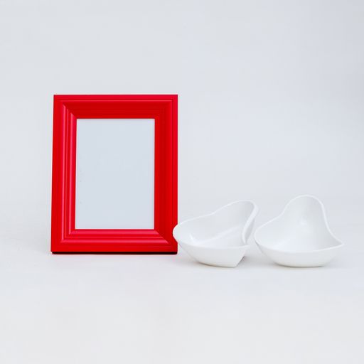 A closeup shot of a white heart-shaped bowl and a red picture frame with copy space
