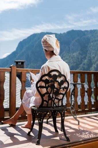 A young female wearing a bathrobe with a towel on her head reading a book on the balcony