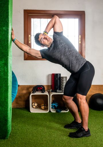 Attractive and muscular Latino man in sportswear doing stretching in the gym after training