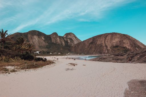 A beach surrounded by the sea and rocks covered in greenery under the sunlight in Brazil
