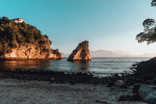 A beach surrounded by the sea and rocks covered in greenery under the sunlight in Brazil