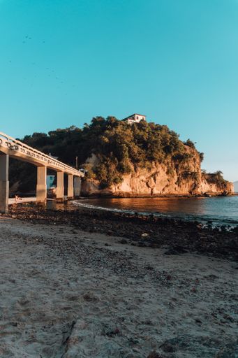 A beach surrounded by the sea and rocks covered in greenery with a bridge in Brazil