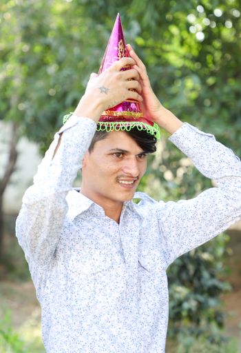 A vertical shot of a South Asian man wearing a birthday hat, outdoors during daylight
