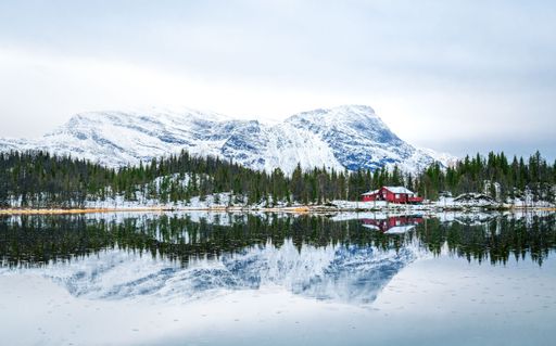 This red cabin sits perched on the edge of a pristine, snow-capped lake, giving onlookers a majestic view of the surrounding countryside