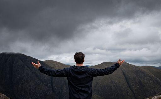 This is a stock photo of a man standing with his arms raised, looking out to a valley