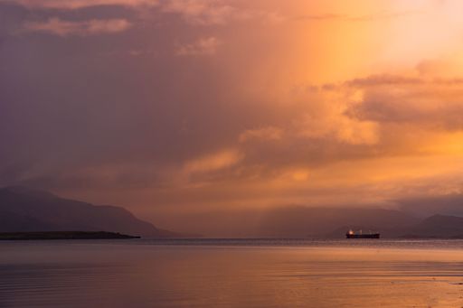 This tranquil image of a boat sitting alone in the still, calm water on a cloudy day could be used for a coastal or maritime theme