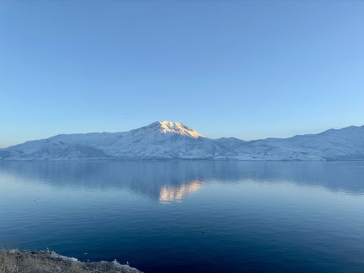 A large body of water is surrounded by snow-covered mountains in the distance