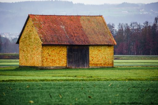 An idyllic, rustic brick barn stands in a lush meadow, silhouetted by a backdrop of tall trees