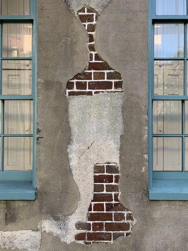 A vertical shot of an old exposed brick wall texture between two glass windows