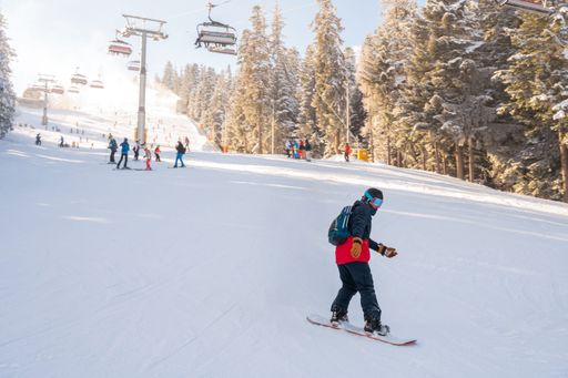 A man with a helmet and backpack skiing on a slope next to a ski lift