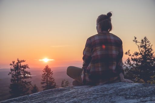 A young hiker sitting on a cliff and enjoying the sunset over a mountain valley