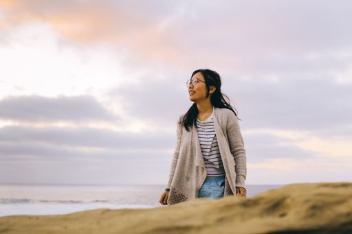 Young adult Asian woman on the beach looking out into the distance.