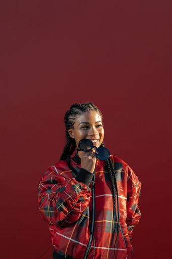 A vertical shot of a cheerful African-American young girl holding sunglasses and smiling on a dark red background