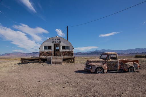 The remnants of a pick-up car and an old building in the middle of a field surrounded by mountains