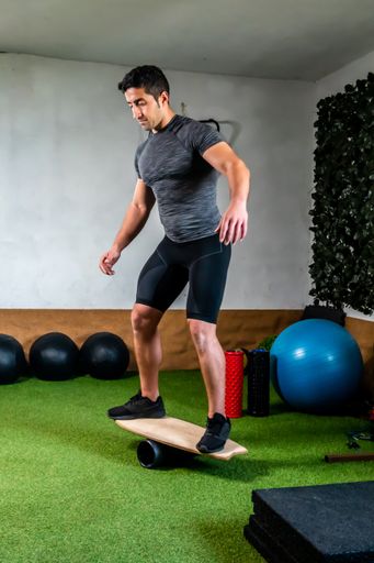 A Hispanic man doing specific surf training working out instability with board and wheel in gym
