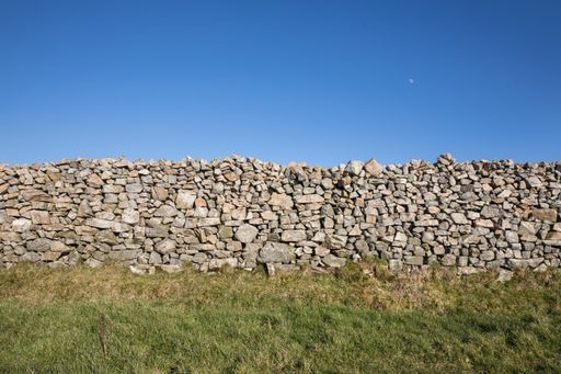 A beautiful shot of stone wall in a green field under a clear sky