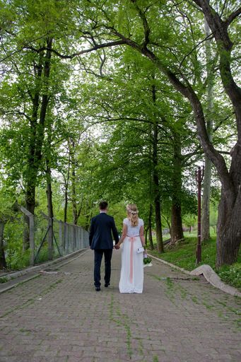 A shallow focus of a newly married couple holding hands and walking in a park