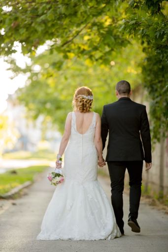 A shallow focus of a newly married couple holding hands and walking through a park