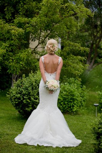 A shallow focus of a blonde bride holding a bouquet of flowers and standing in a garden