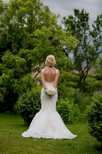 A shallow focus of a blonde bride holding a bouquet of flowers and standing in a garden