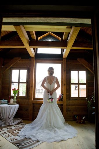 A vertical shot of a blonde bride holding a flower bouquet and looking out of the window of a wooden cab