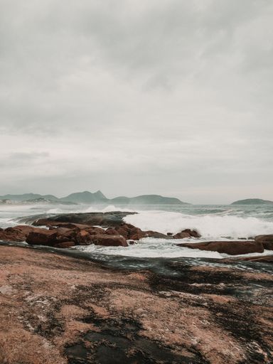 A vertical shot of the waves of the sea hitting the cliffs on the beach captured on a cloudy day